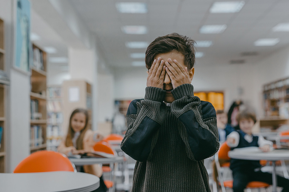 Boy standing in classroom, covering his eyes